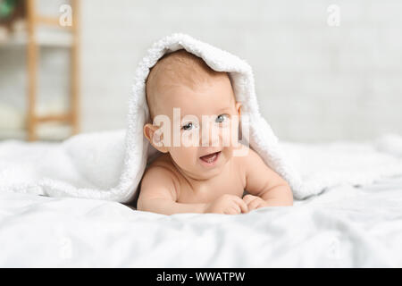 Happy little baby crawling on bed under blanket Stock Photo
