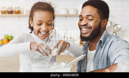 Cute black girl adding eggs into dough bowl Stock Photo