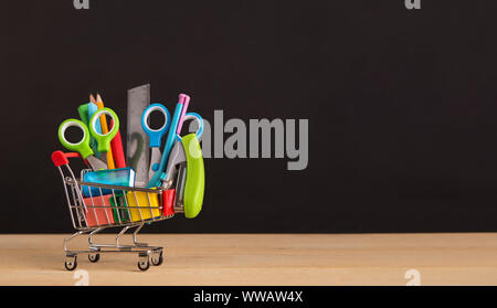 Shopping cart with school supplies over chalkboard background Stock Photo