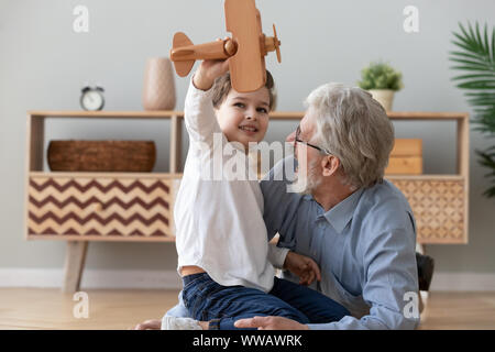 Happy old grandfather and cute grandson playing with wooden plane Stock Photo