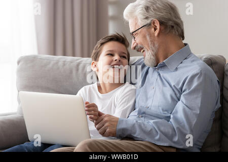 Happy old grandfather and grandson laughing using laptop on sofa Stock Photo