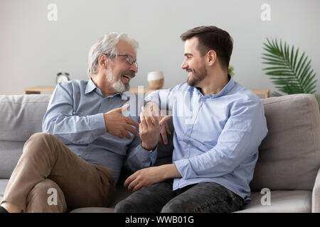 Happy old father and young son talking sit on sofa Stock Photo