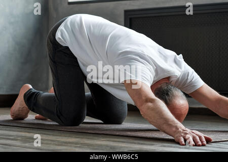 Stretching spine asana. Senior man practicing yoga at home and standing in extended puppy pose Stock Photo