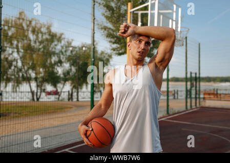 Tired basketball player with ball on outdoor court Stock Photo