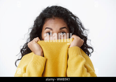 Girl prepared for winter. Carefree pretty african american woman, curly hair, hiding face in yellow sweater, raise eyebrows and look camera playfully Stock Photo