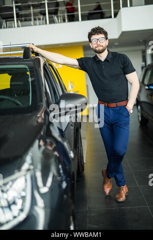 Visiting car dealership. Handsome man is stroking his new car and smiling Stock Photo