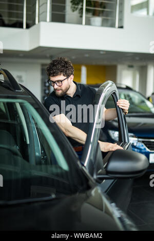 Visiting car dealership. Handsome man is stroking his new car and smiling Stock Photo