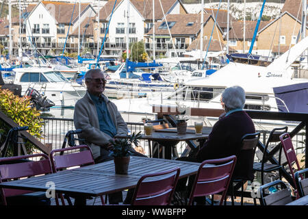 An elderly couple enjoying a drink outside in a restaurant at a yacht marina Stock Photo
