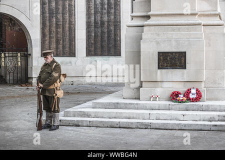 A man in World war one soldiers uniform standing next to a British war memorial with red poppy wreaths laid on it Stock Photo