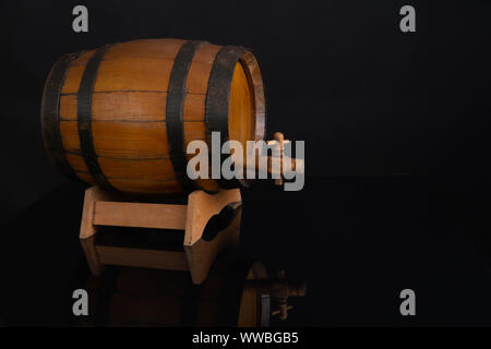 Wooden barrel with tap on a black mirror. Black background behind.. Stock Photo