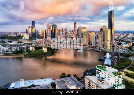 Story bridge in Brisbane city over Brisbane river in front of high-rise business towers and apartment buildings at sunrise in elevated aerial view. Stock Photo