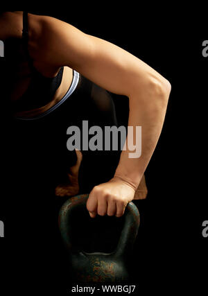 young girl of athletic appearance with black hair is pushing up from an iron kettlebell from a lying position, low key Stock Photo