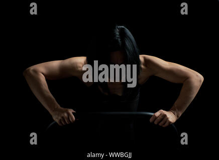 young girl of athletic appearance with black hair is pushing up from the surface on a dark background, athlete’s muscular body is tense Stock Photo