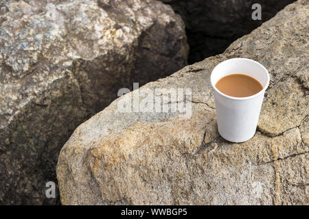 A cardboard - paper cup of coffee placed on the stones of a jetty in