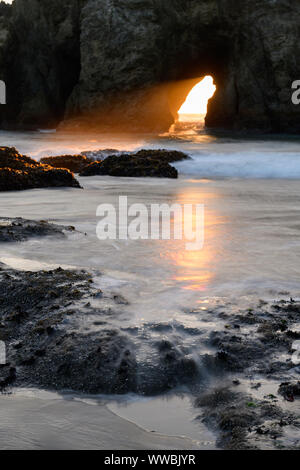 The sun sets through Harris Creek State Park sea arch just north of Brookings, Oregon, North America along the Pacific coast.
