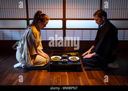 Young couple seiza sitting on hardwood floor pillows at traditional Japanese in ryokan kaiseki dishes of soba noodles, natto, edamame and soy sauce on Stock Photo