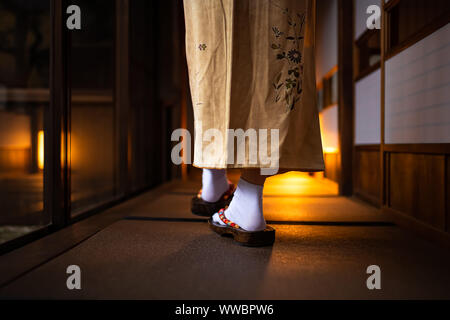 Traditional Japanese home or ryoka with tatami mat floor, shoji sliding paper doors, back of woman feet in kimono and geta shoes tabi socks walking in Stock Photo