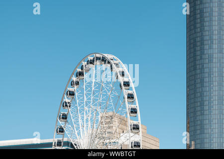 Atlanta, USA - April 20, 2018: Skyview Atlanta ferris wheel in Centennial Olympic park with office building skyscrapers and blue sky in background in Stock Photo