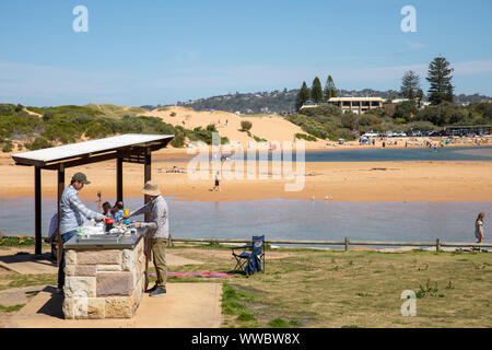 Two australian men cooking on a beach barbecue barbecue in Narrabeen on Sydney northern beaches, New South Wales,Australia Stock Photo