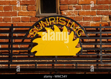 Sunrising sign in metal bench in front of red brick wall Stock Photo