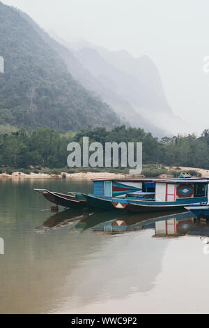 Traditional Laotian wooden slow boat on Nam Ou river near Nong Khiaw village, Laos. Reflection in water Stock Photo