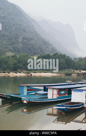 Traditional Laotian wooden slow boat on Nam Ou river near Nong Khiaw village, Laos. Reflection in water Stock Photo