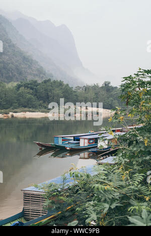 Traditional Laotian wooden slow boat on Nam Ou river near Nong Khiaw village, Laos. Reflection in water Stock Photo