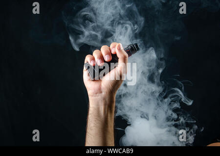 hand holding vape e-cigarette or electronic cigarette with white smoke over a black background. Stock Photo