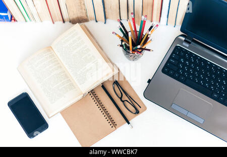 Open textbook, notebook, smartphone, laptop computer, stack of books education back to school background, glasses and pencils in plastic holder with c Stock Photo