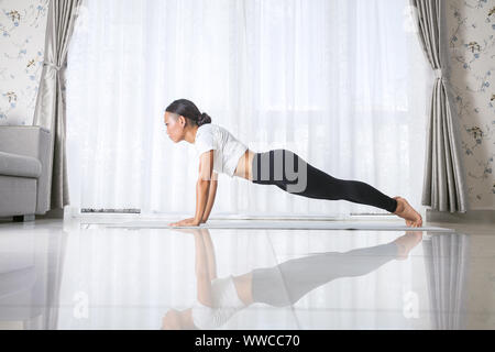 Attractive young asian woman exercising and sitting in yoga position while resting at home