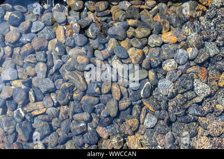 Texture of wet pebbles. Smooth pebbles under clear water. Striped stones at the bottom underwater create a fresh Abstract background. Stock Photo