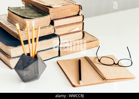Stack of old books, open notebook, glasses and pencils in holder, education concept background, many books piles with copy space for text Stock Photo