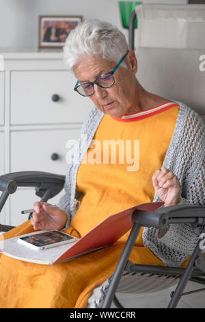 An elderly person uses a mobile phone by reading notes Stock Photo