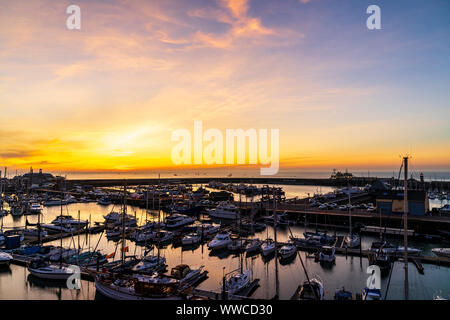 Dawn sky over the English Channel and the harbour at the coastal town of Ramsgate on the Kent coast in England. Harbour and yachting marina with a thin band off orange yellow on the horizon just before sunrise, turning into blue sky with some wispy clouds. Stock Photo