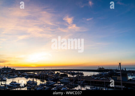 Dawn sky over the English Channel and the harbour at the coastal town of Ramsgate on the Kent coast in England. Harbour and yachting marina with a thin band off orange yellow on the horizon just before sunrise, turning into blue sky with some wispy clouds. Stock Photo