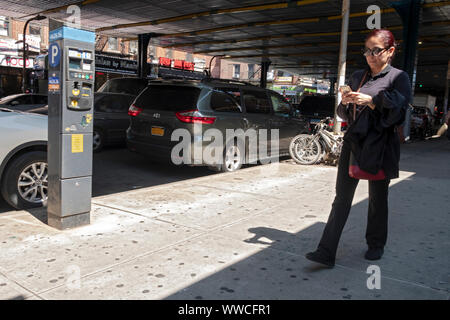 A middle aged woman checking her cell phone while walking under the elevated subway . In Jackson Heights, Queens, New York City. Stock Photo