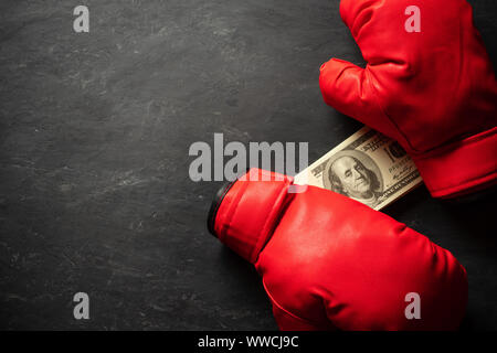 Boxing Gloves holds the dollar banknote on black cement background. Concept of boxing betting or business struggle. Top view and copy space for text. Stock Photo