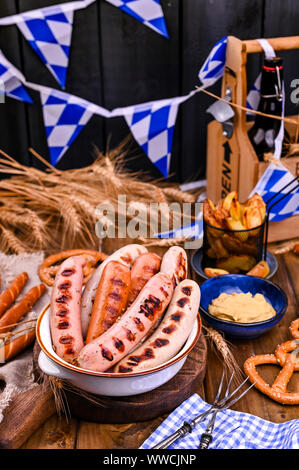 German sausages on the grill. Traditional German sausages and pastry brezel for a beer festival. Wood background and decor  Stock Photo