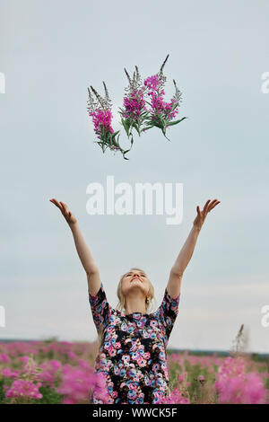 Pregnant girl walking in field of flowers fireweed, woman smiling and picking flowers. The girl is expecting the birth of a baby in the ninth month of
