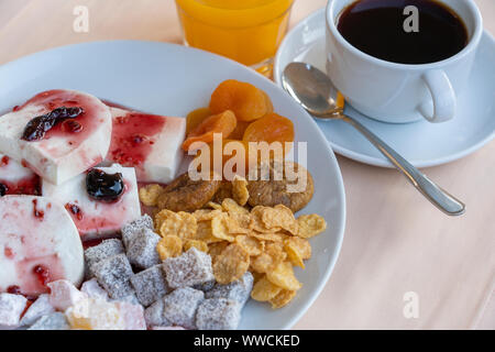 Curd cheese poured fruit yogurt, dried apricots, figs, cornflakes and cup coffee on table. Breakfast concept. Close up Stock Photo
