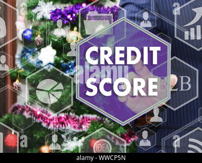 The businessman chooses CREDIT SCORE on the touch screen, the backdrop of the Christmas tree and decorations. Special toning . Stock Photo
