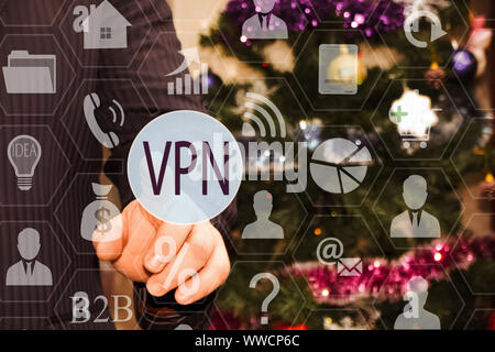 The businessman chooses a VPN on the touch screen, the backdrop of the Christmas tree and decorations Stock Photo