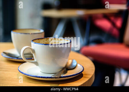 Two empty cups of coffee latte on cafe table. Chairs on background. Electric light Stock Photo