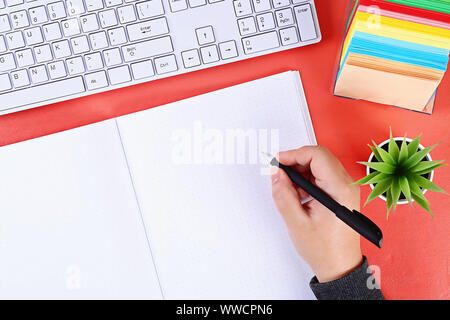 Blank notebook on the coral background, plant, keyboard. Top view, flat lay. Mockup, copy space. Stock Photo