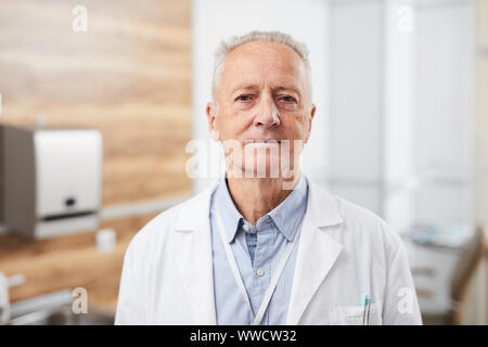 Waist up portrait of senior doctor smiling calmly looking at camera while posing in office of modern clinic, copy space Stock Photo