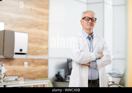 Portrait of confident senior doctor looking at camera while posing standing in office of modern clinic, copy space Stock Photo