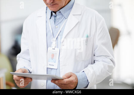 Mid section portrait of unrecognizable senior doctor holding digital tablet while standing in office of modern clinic and using internet, copy space Stock Photo