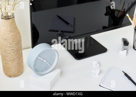 Modern workspace background, front view. Mockup workplace with desktop, clock, office supplies and flower branch in vase Stock Photo