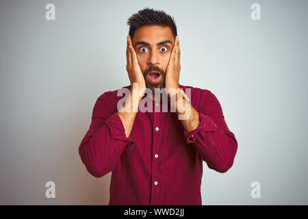 Young indian man wearing red elegant shirt standing over isolated grey background afraid and shocked, surprise and amazed expression with hands on fac Stock Photo