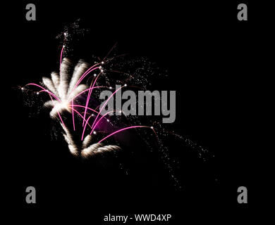 Fireworks burst in white and pink sparkling in the dark night sky. Stock Photo